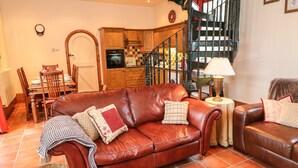 A cozy living room with a brown leather sofa, a dining table with chairs, a kitchen area, and a staircase. - The Old Chapel (Chesterfield)