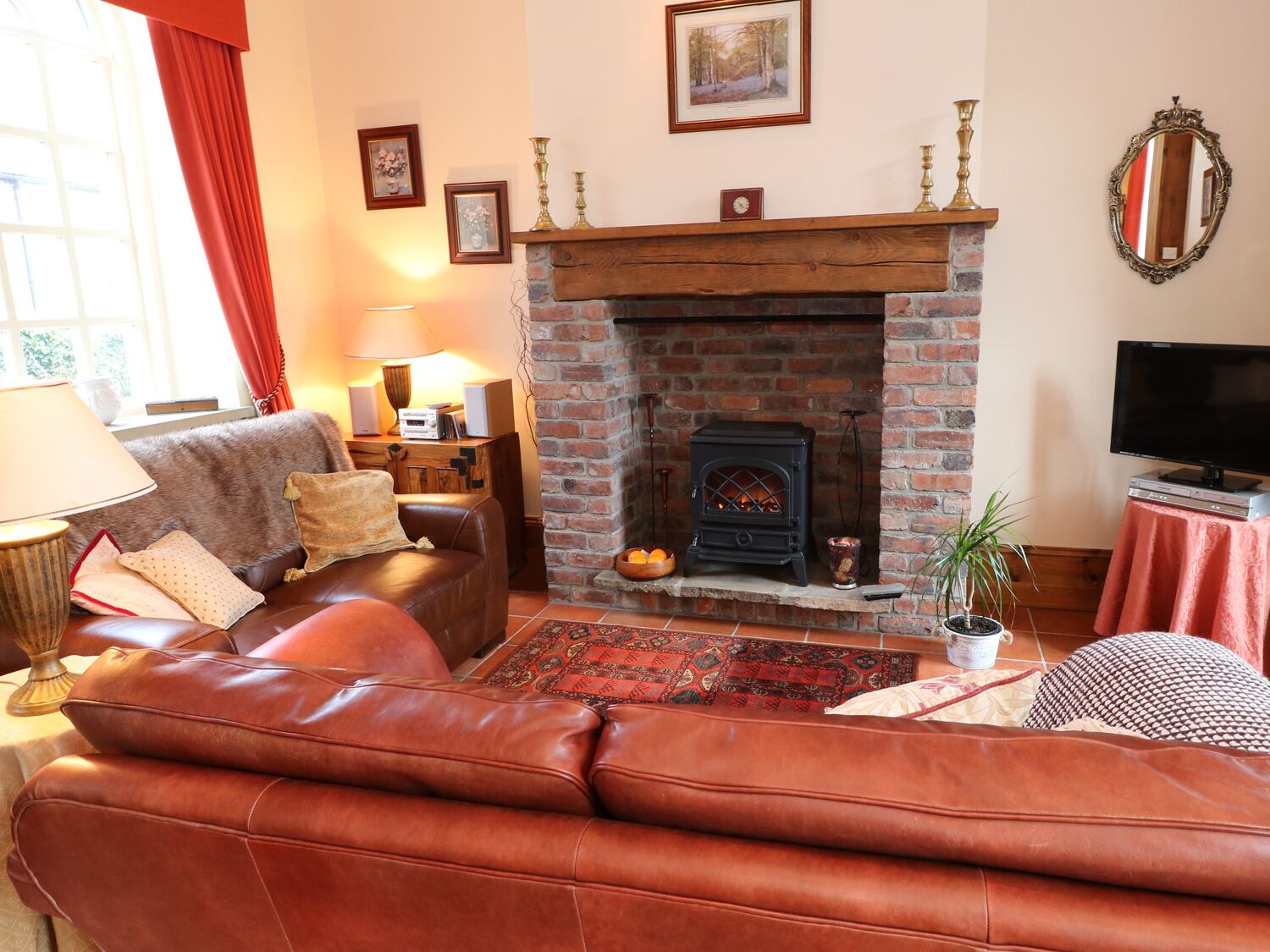 A cozy living room with a leather sofa, a fireplace, a television, and a red curtain.