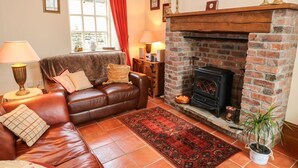 A cozy living room with a leather sofa, a fireplace, and a large window with curtains. - The Old Chapel (Chesterfield)