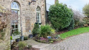 A stone building with arched windows and a well-maintained garden with various plants and a large tree. - The Old Chapel (Chesterfield)