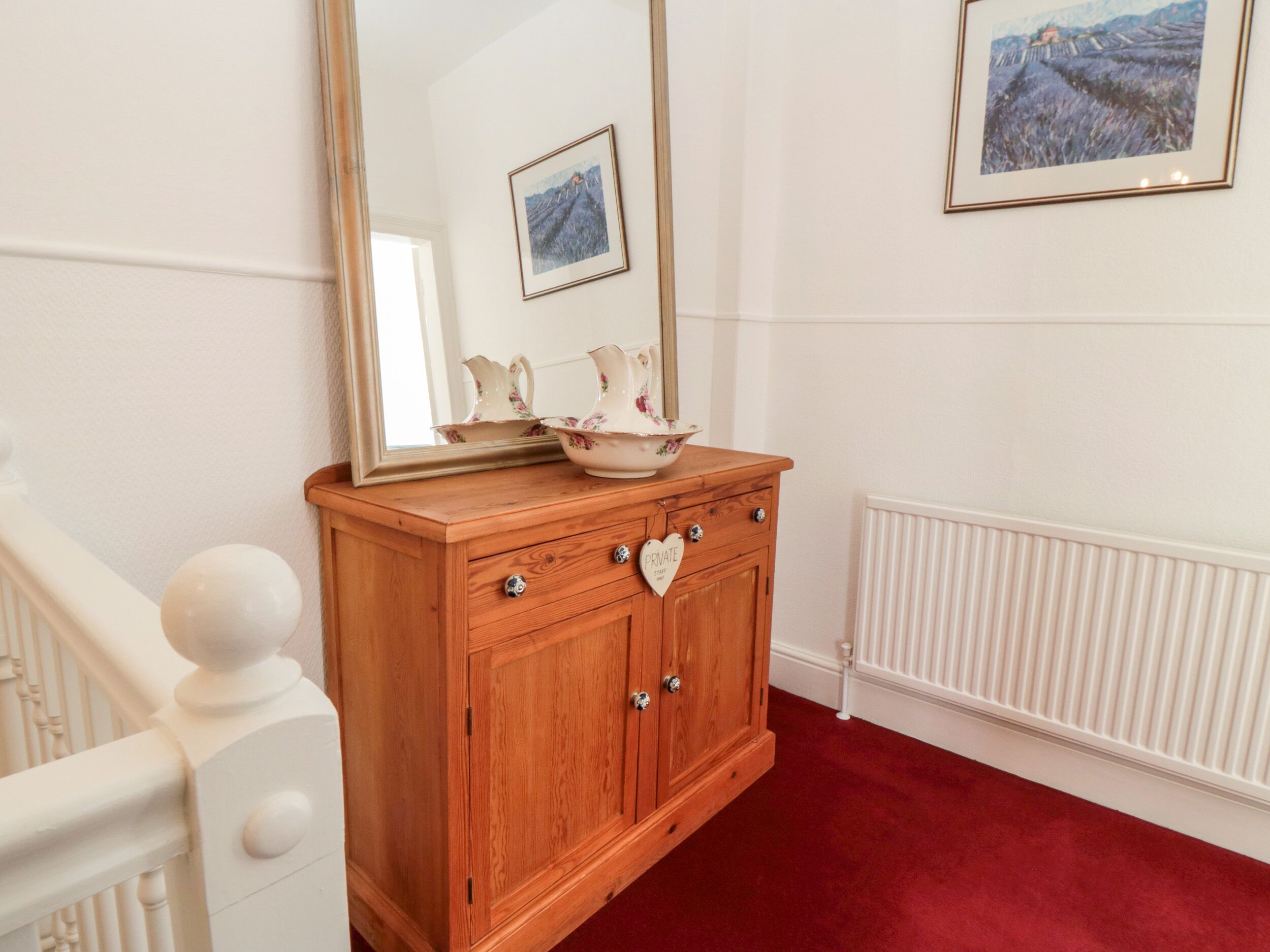 A wooden cabinet with a mirror, a floral pitcher, and a heart-shaped decoration.