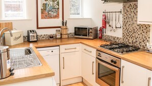 Una cocina moderna equipada con lavavajillas, tostadora, microondas, estufa, horno y pileta. Se observan armarios, una ventana y un cuadro en la pared.