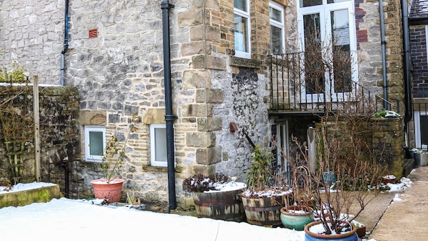 Un edificio de piedra con varias ventanas, un balcón y macetas con plantas.
