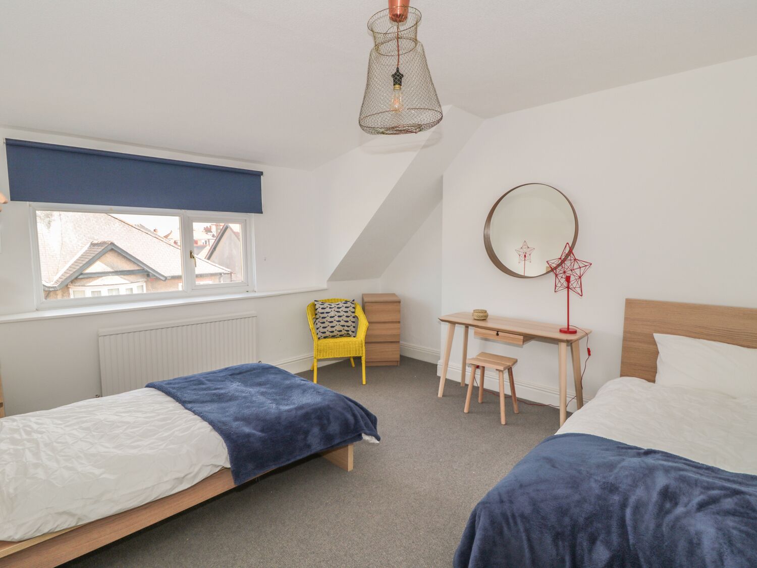 Een slaapkamer met twee bedden, een bureau, een stoel, een raam en een hanglamp.