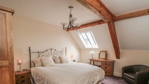 A bedroom with a large bed, a desk, a chair, a nightstand, a lamp, and a skylight. - New Stable Cottage (Whitby)