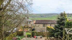 A stone house with a tiled roof, surrounded by a garden with various plants and a wooden fence. - New Stable Cottage (Whitby)