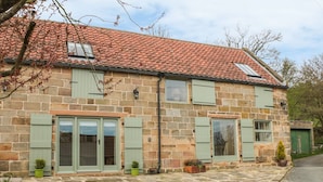 A stone building with a tiled roof, green shutters, and a stone-paved entrance. - New Stable Cottage (Whitby)