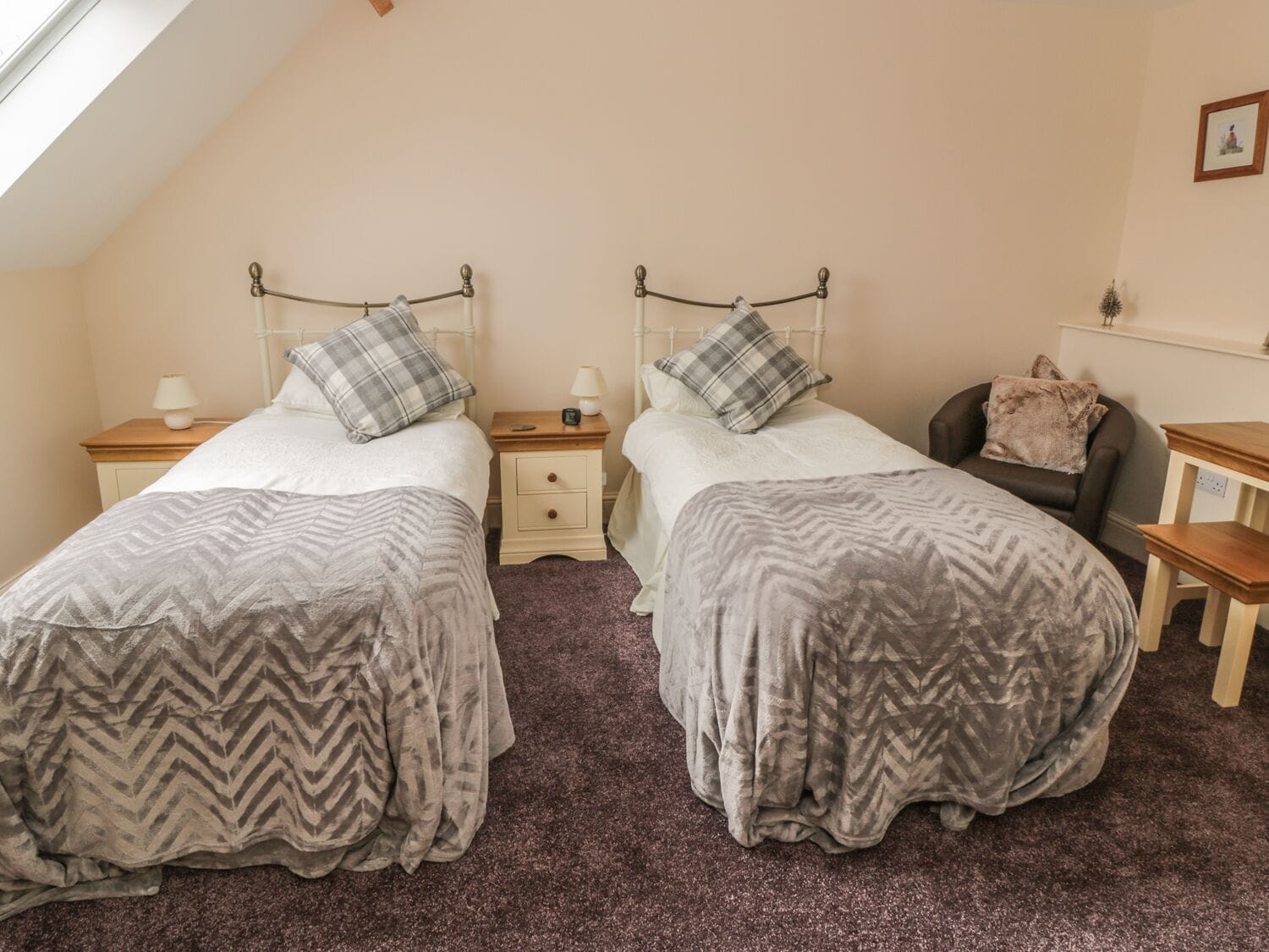 A bedroom with two twin beds, a nightstand with a lamp, a chair, and a small table.