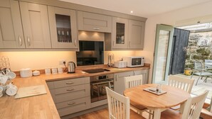 A modern kitchen with wooden countertops, stainless steel appliances, and a dining area with white chairs. - New Stable Cottage (Whitby)