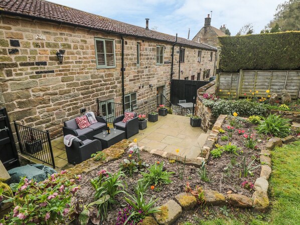 A stone building with a patio area featuring outdoor seating and a flower garden.