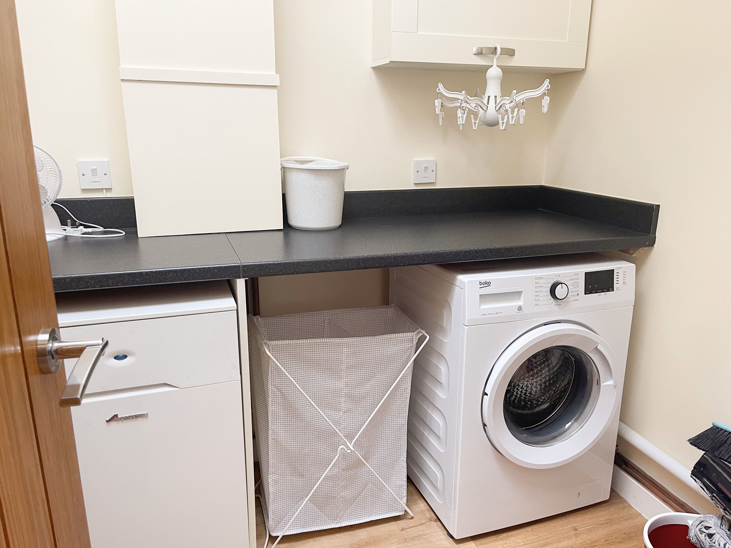 A compact laundry area with a washing machine, a drying rack, and a small cabinet.