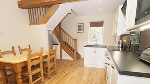 A kitchen with wooden flooring, white cabinets, a built-in oven, and a wooden dining table with chairs. - The Coach House (Llanrwst)