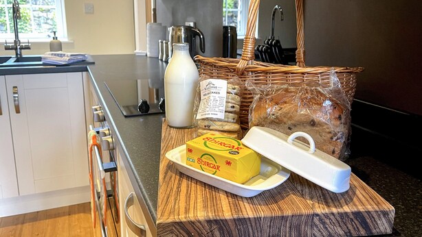 A kitchen counter with a loaf of bread, a bottle of milk, a box of Shira cheese, and a wicker basket. - The Coach House (Llanrwst)