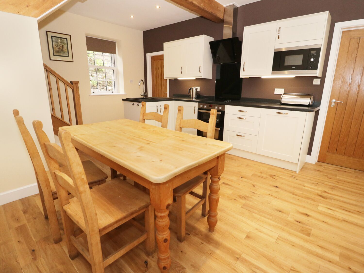 A compact kitchen with white cabinets, a black microwave, and a wooden dining table with chairs.