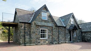 A stone building with a pitched roof and a brick-paved courtyard. - The Coach House (Llanrwst)