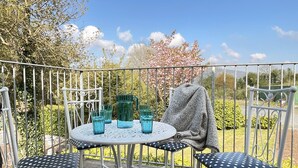 A round table with four blue chairs, a metal fence, and a garden with trees and bushes. - The Coach House (Llanrwst)