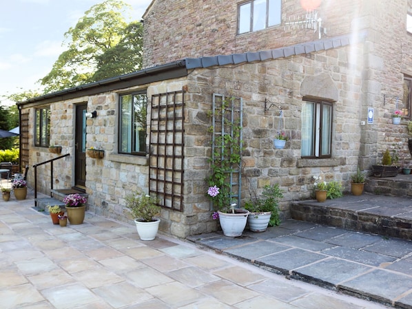 A stone building with a small porch, potted plants, and a wooden trellis.
