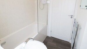 Une salle de bain avec une douche à parois de verre, des toilettes blanches et une porte blanche avec une plaque bleue.