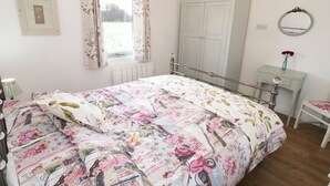 Une chambre à coucher comprenant un lit, une armoire, une table de chevet, un miroir et une fenêtre avec des rideaux.