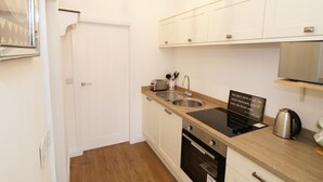 Une cuisine compacte avec des meubles blancs, un plan de travail en bois, un four encastré, un évier et une bouilloire.