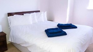 A neatly made bed with white bedding and two folded blue towels on the bed.