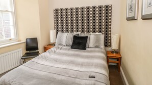 A neatly arranged bedroom with a bed, two bedside tables, a chair, and a radiator. - Apartment 2 (Tenby)
