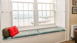 A bay window with a bench, a red pillow, and a view of the sea. - Apartment 2 (Tenby)
