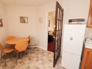 A compact kitchen with a dining area, a refrigerator, and a clock on the wall. - Harbour Side (Maryport)