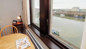 A room with a view of a harbor, a table with a book, a lamp, and a chair. - Harbour Side (Maryport)