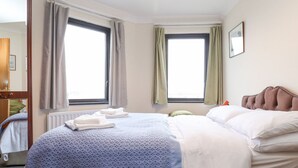 A hotel room with two beds, a large window, a radiator, and a mirror. - Harbour Side (Maryport)