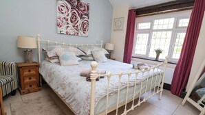 A bedroom with a bed, bedside tables, a chair, a window with curtains, and a wall decoration. - Ty Cerrig (Rhyl)