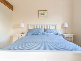 Una cama con ropa de cama azul y blanca a rayas, dos mesitas de noche con lámparas y un cuadro en la pared.