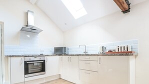 A modern kitchen with white cabinets, a built-in oven, a microwave, and a wooden ceiling beam. - Granary 2 (Hereford)