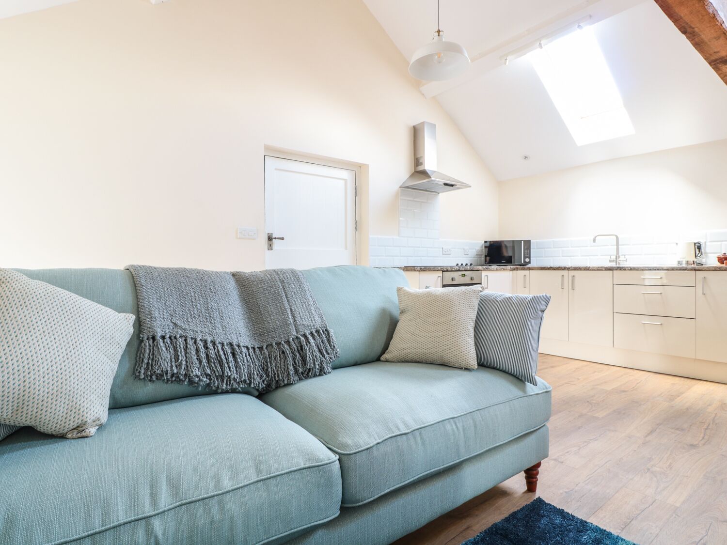 A modern living room with a light blue sofa, a kitchen in the background, and a skylight above.