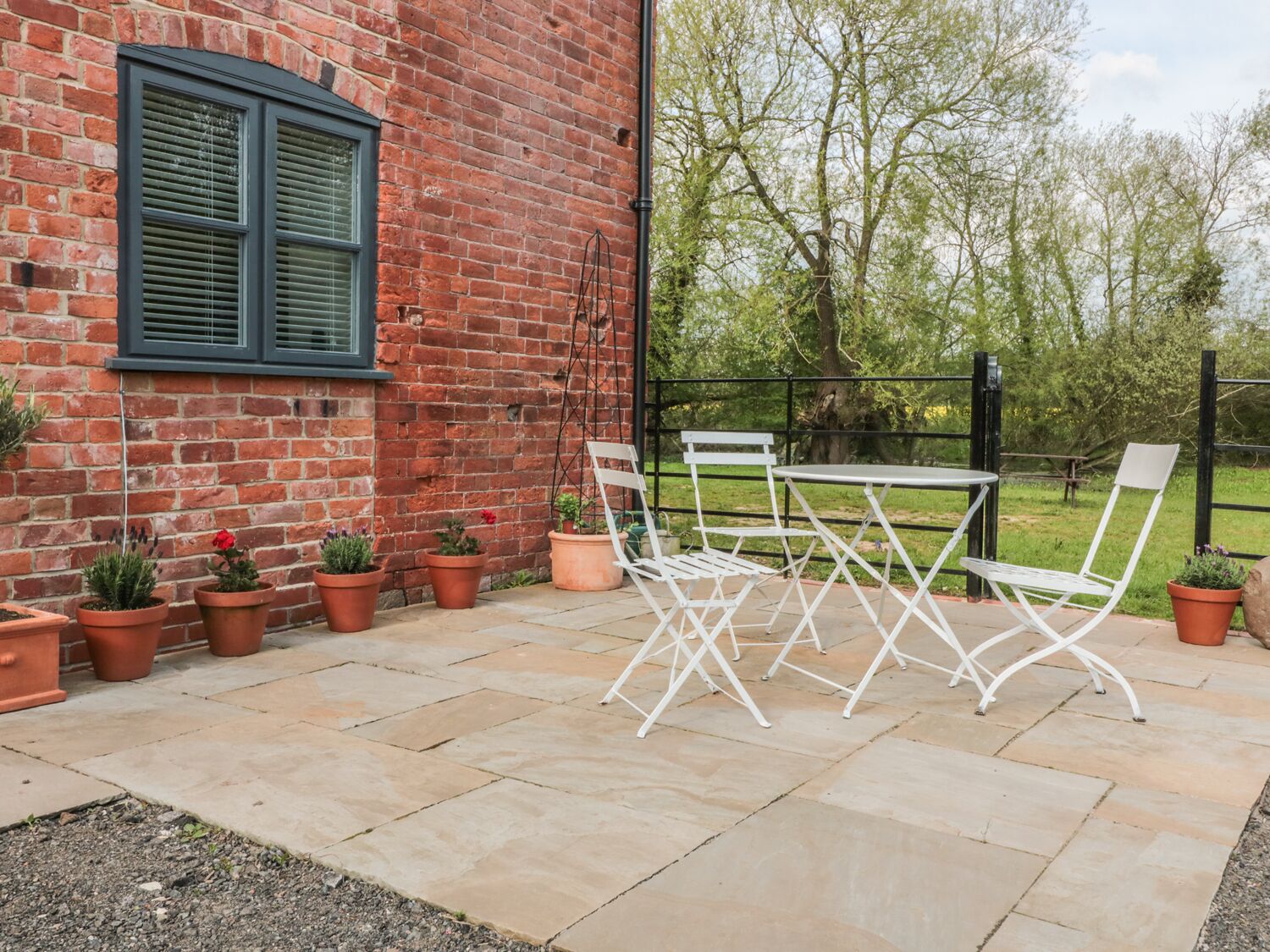An outdoor patio with a brick wall, a table and chairs, and potted plants.