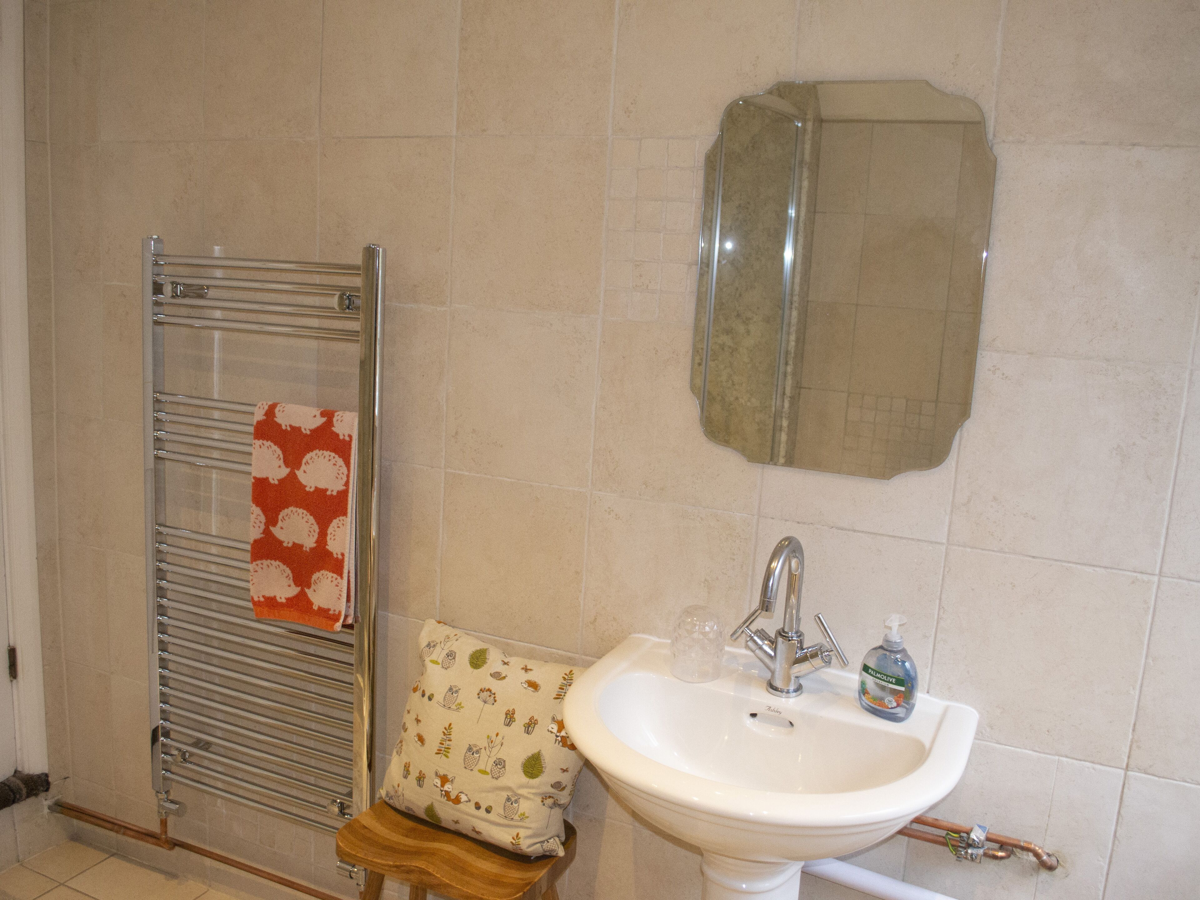 A bathroom with a white sink, a mirror, a towel rack, and a small stool with a cushion.