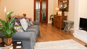 A living room with a grey sofa, a wooden cabinet, a TV stand, and a dining area with a table set for two. - 17 Riverside (Stoke-on-Trent)