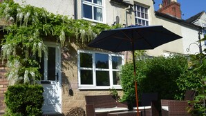 A patio with wicker furniture, a white umbrella, and a house with a brick facade and white window frames. - 17 Riverside (Stoke-on-Trent)