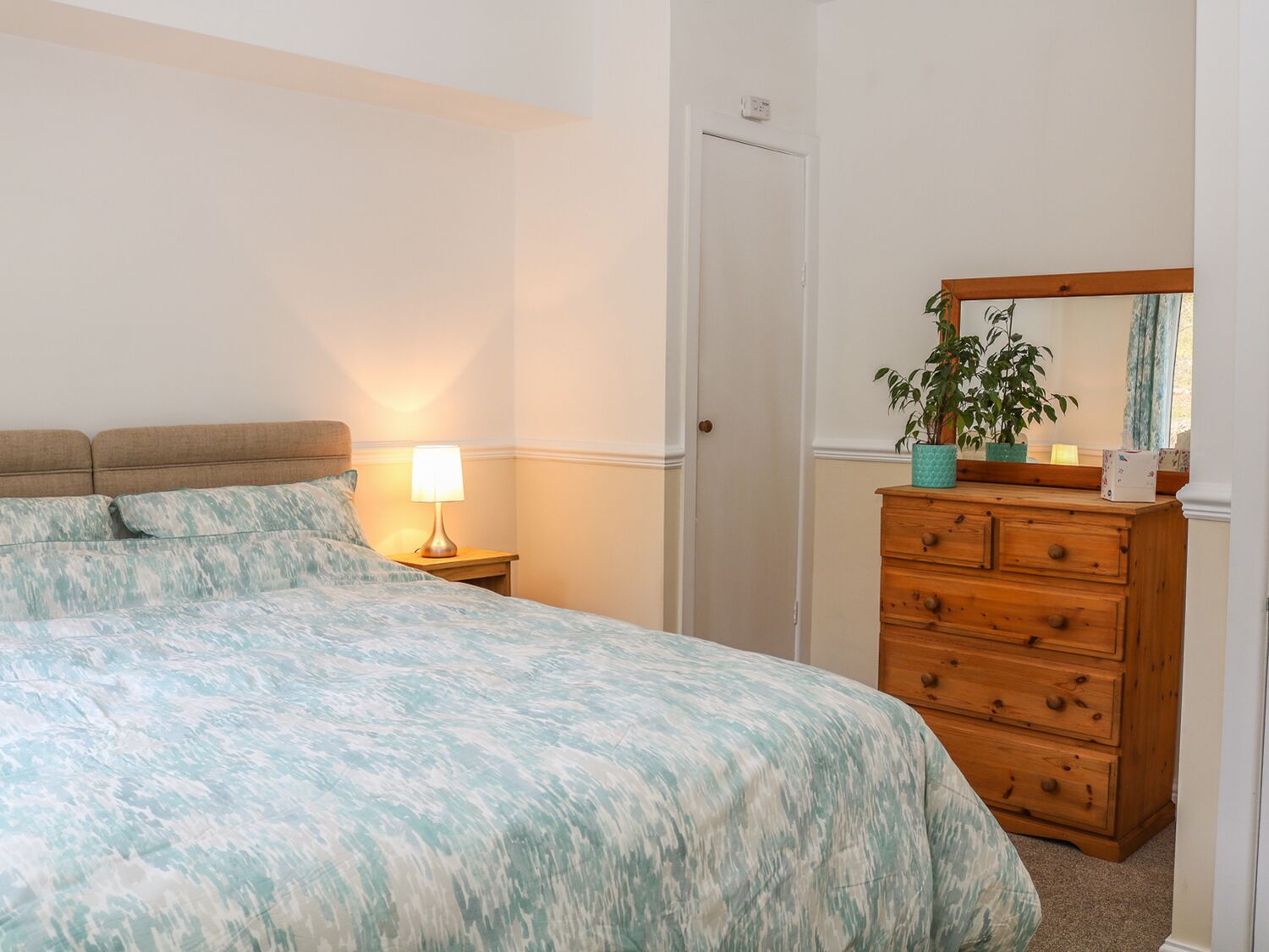 A bedroom with a bed, a nightstand with a lamp, a dresser, and a mirror.
