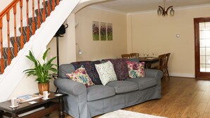 A living room with a grey sofa, a wooden staircase, a dining area with a table and chairs, and a potted plant. - 17 Riverside (Stoke-on-Trent)