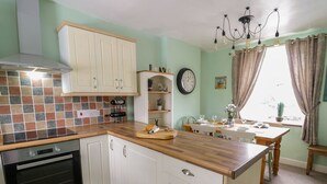 Une cuisine avec des armoires blanches, un four encastré, un plan de travail en bois et un coin repas avec une table mise pour deux personnes.