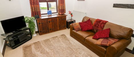 A living room with a brown leather sofa, a wooden cabinet, a television on a stand, and a window with curtains.