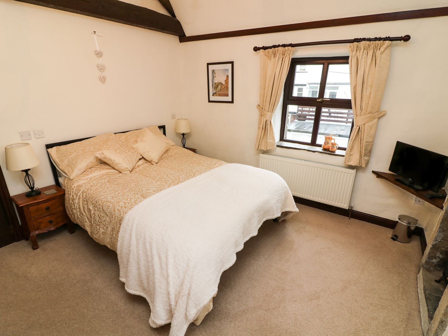 A bedroom with a bed, bedside lamps, a window with curtains, a radiator, and a television on a stand.