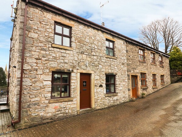 A stone building with multiple windows and doors, a sloped roof, and a brick-paved street.