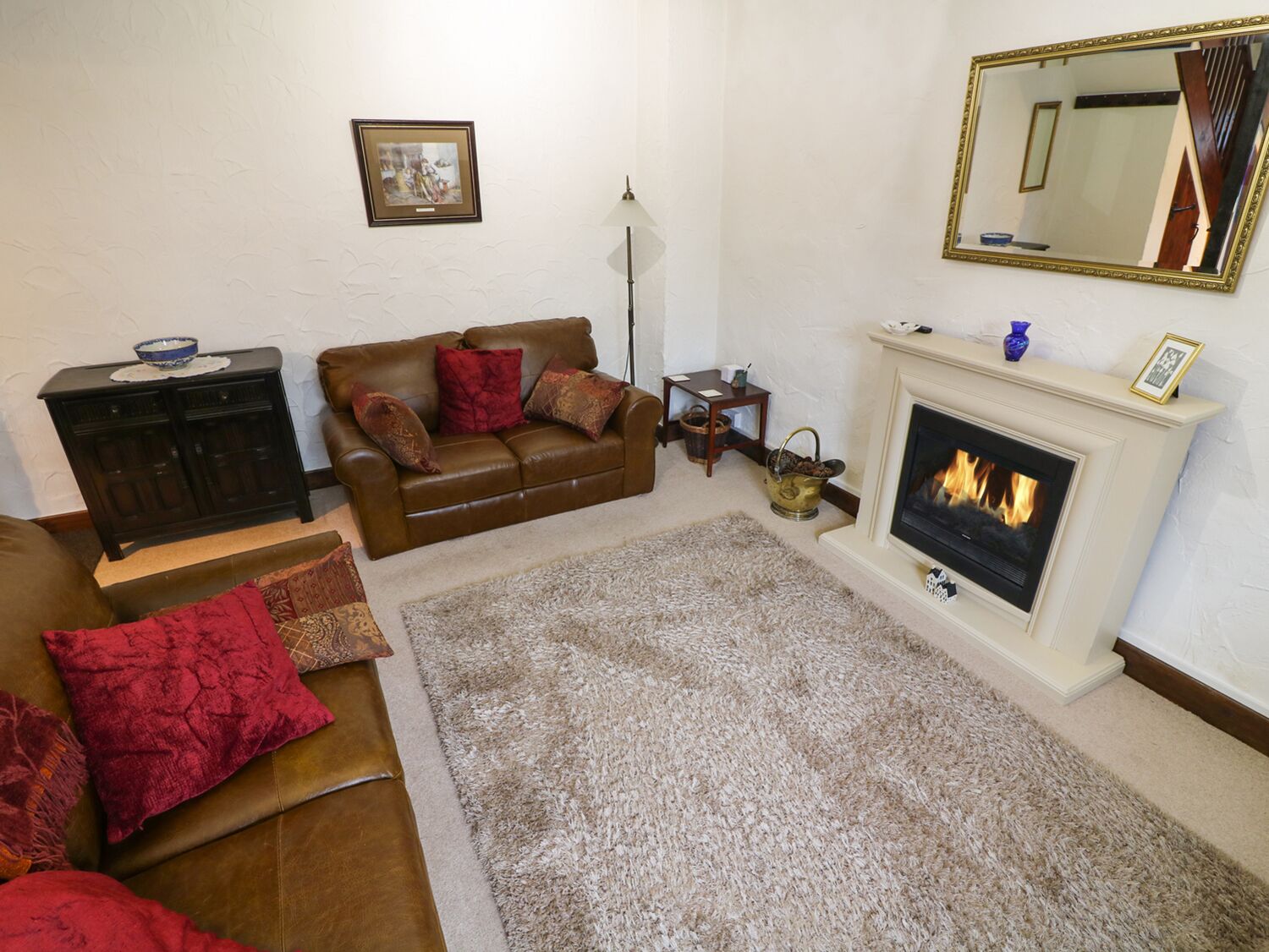 Una sala de estar con un sofá de cuero marrón, un cojín rojo, una chimenea blanca y un cuadro en la pared.
