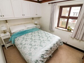 A bedroom with a bed, white cabinets, a window with curtains, and a radiator.