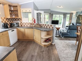 A modern kitchen with wooden cabinets, a built-in microwave, and a dishwasher. There is a seating area with a sofa and a television.