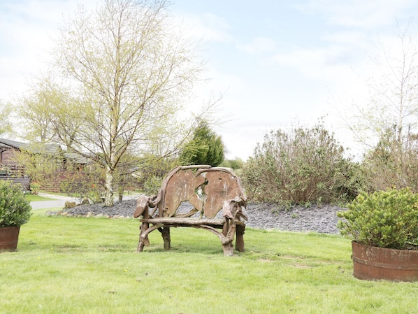 A rustic outdoor sculpture in a grassy area with trees and a building in the background. - 16 Badgers Retreat (Richmond)