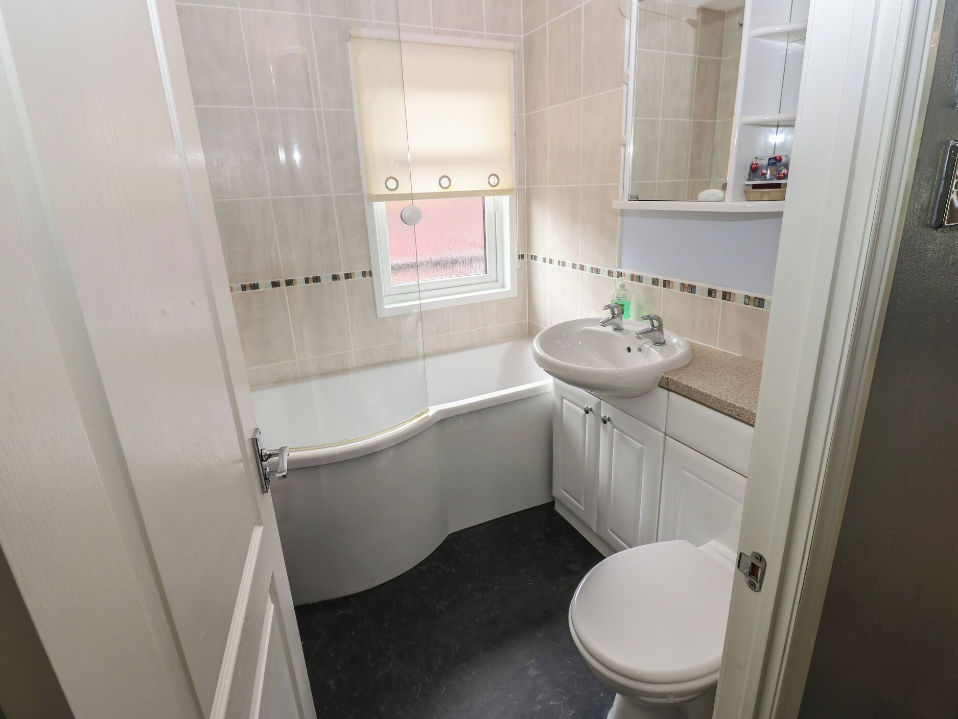 Un baño con inodoro blanco, lavamanos, bañera y ventana con persiana.