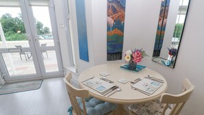A dining area with a round table set for four, wooden chairs with cushions, a vase with flowers, and a large mirror on the wall. - Beachcomber (Marazion)